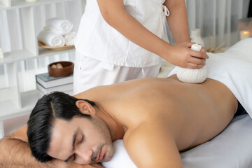 Hot herbal ball spa massage body treatment, masseur gently compresses herb bag on man body....
