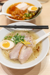 A close up duck ramen noodle and spicy chili ramen with duck slice and boil egg decorate with chop spring onion with chopstick and spoon in in tall ramen bowl