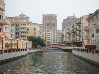 A view of a tranquil canal surrounded by colorful European-style buildings, with a small bridge in...