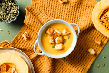 Pumpkin soup with croutons and seeds on orange towel. Cozy autumn food