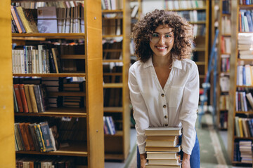 Young student holding a pile of books in the library