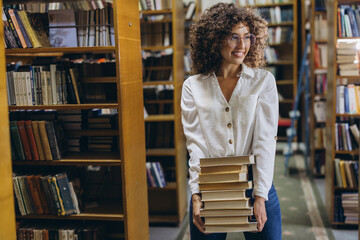 Young student carrying a pile of books in the library