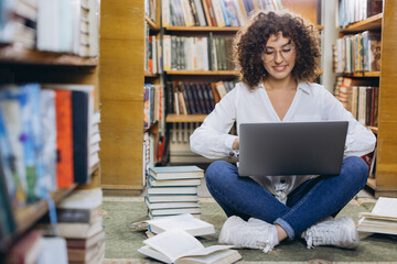 Young student using laptop surrounded by books in library