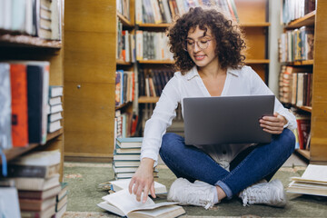 Student researching using laptop and books in library