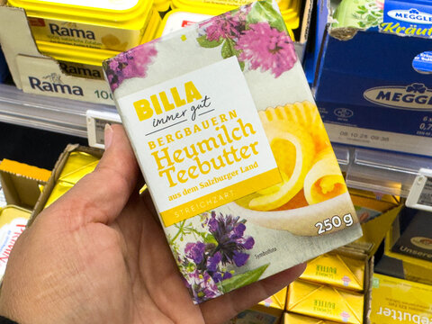 Villach, Austria - August 21, 2025: BILLA Heumilch Teebutter packaging held in hand, showcasing vibrant design with floral elements and butter details in grocery store aisle