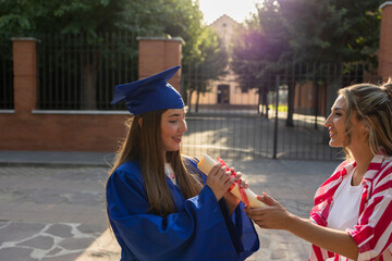 Proud graduate receiving diploma from friend outdoors after university ceremony
