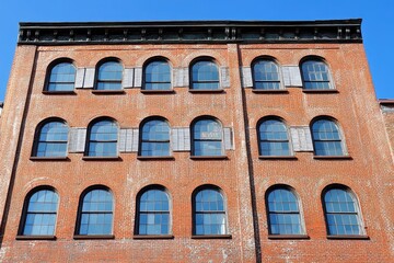Obraz premium Renovated 19th Century Warehouse in Brooklyn, NYC: Arched Windows and Metal Shutters Beneath Clear Blue Skies