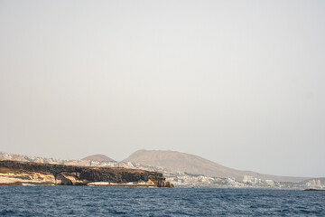Coastal landscape with distant mountains and calm ocean horizon under clear sky
