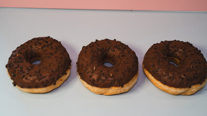 Three rich chocolate donuts with glossy glaze, captured in a close-up to showcase their decadent texture and appeal. Ideal for dessert menus, bakery promotions, and social media content.