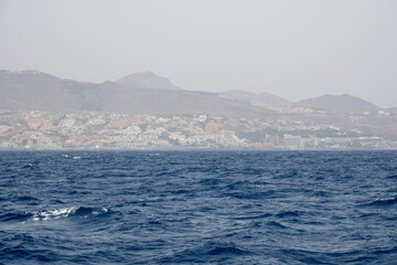 Coastal cityscape with mountain background and choppy blue sea under cloudy sky