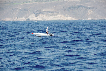 Solitary fisherman on calm ocean waves with mountain views in the distance