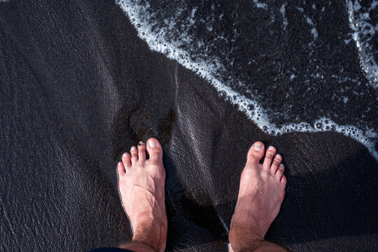 Bare feet on black sand beach with ocean waves - Powered by Adobe