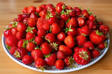 Fresh juicy strawberries in a plate on a wooden table in daylight