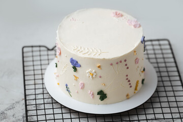 Beautiful birthday cake with white chocolate icing on the grey pastel background decorated with cream flowers
