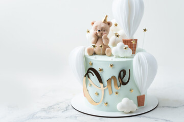 Birthday cake frosted with turquoise chocolate velvet coating and decorated with edible teddy bear figure and balloons on top. Cute birthday cake for a little one year old baby boy on white background © alexanderon