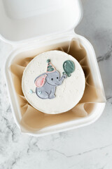 Little birthday bento cake with white cream cheese frosting decorated with funny elephant drawing in a white gift box