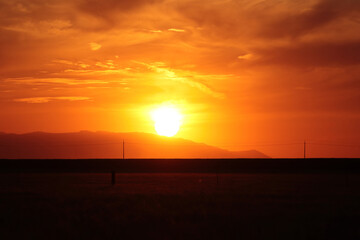 Fototapeta premium The bright red sun sets behind the blazing horizon