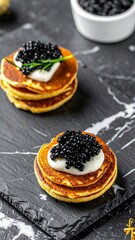 Luxury black caviar with mini pancakes and sour cream on dark marble, holiday party appetizer, gourmet blini canap&eacute;s, New Year celebration, elegant dining