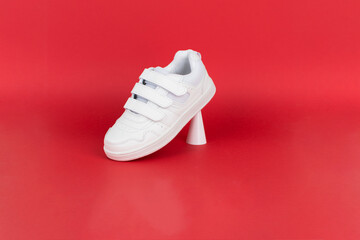 White children's sneakers on red background. Minimal background