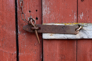 Rusty old latch and chain lock securing a weathered red wooden shed door, showing the passage of time and rustic charm in every detail