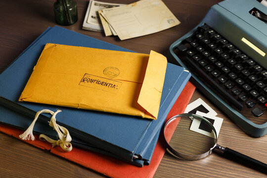 Investigator desk with vintage documents. Yellow envelope with confidential stamp. Vintage typewriter, magnifying glass.