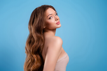 Portrait of a charming woman with long wavy brown hair on a blue background, exuding beauty and...