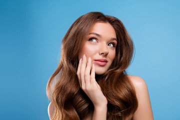 Fototapeta premium Charming young woman with long wavy brown hair posing against a blue background, showing natural beauty