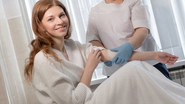 A beautiful young woman in a bathrobe undergoing blood collection procedures for analysis or plasmolifting procedures, interior of a hospital room, health and self-care, concept