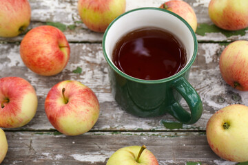 Green mug with hot apple tea surrounded by fresh apples on rustic wooden table