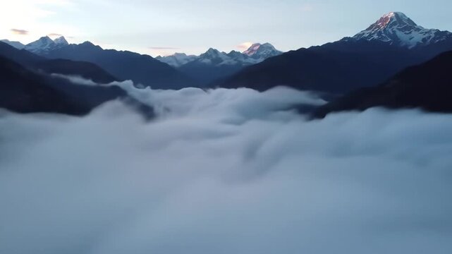 Stunning aerial view of a mountain range with snow-capped peaks rising above a vast sea of clouds in a valley.