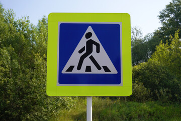 Pedestrian crossing sign warns drivers in rural area with lush green vegetation