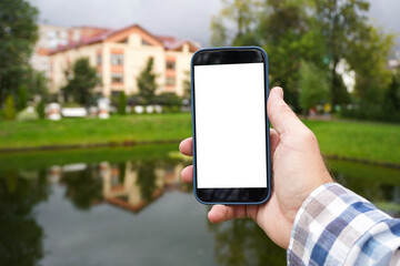 Man holding smartphone with white screen in park near lake
