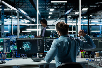 Data center engineer stretching at workstation to relieve back fatigue while using AI LLM assistant...