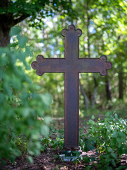A metal cemetery cross stands among the trees in the forest. Summer season.