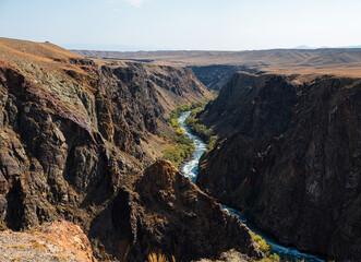A mountain river flows through the bottom of the canyon, Majestic Kazakh canyon landscape with vibrant red rock formations and winding natural paths