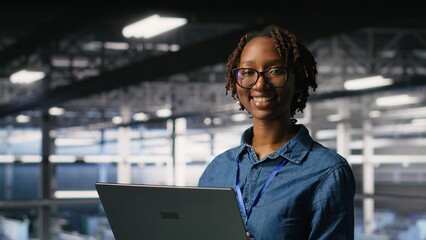 Happy woman in data center doing maintenance tasks on laptop, ensuring optimal performance. Engineering team reviewing diagnostics and applying patches to server room, improving stability