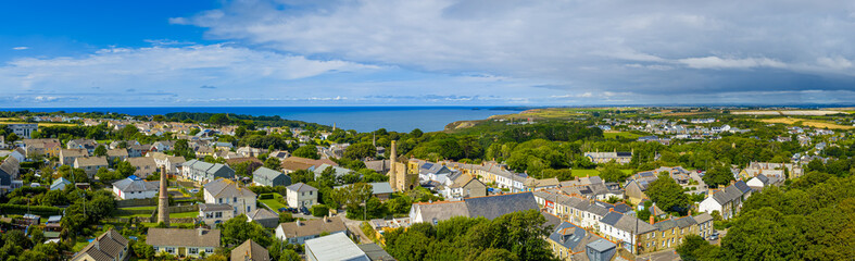 Obraz premium Aerial view of St Agnes village in Cornwall, England, with stone houses, church spire, lush greenery, and coastline in the background