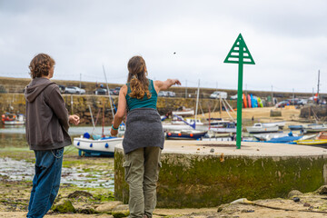 Fishing boats resting on seaweed-covered ground at low tide in Mousehole harbour, Cornwall, with stone pier and parked cars in background
