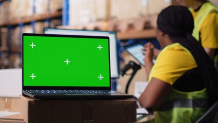 Warehouse staff works next to green screen on computer display, managing shipping labels and order fulfillment or e-commerce inventory systems in industrial storage room. Camera B.
