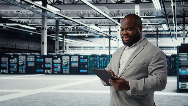 System administrator in data center workplace uses tablet to calibrate energy usage. Server farm IT expert using device to inspect UPS configurations, doing maintenance on equipment, camera A