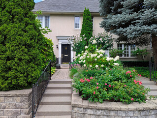 Long path to front door of house, surrounded by flowers and evergreen shrubbery