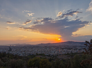 Scenic view of a sprawling city at sunset with mountains in the background and dramatic clouds