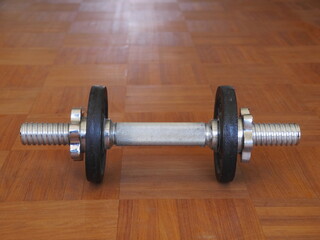 Silver dumbbell is sitting on a wooden floor
