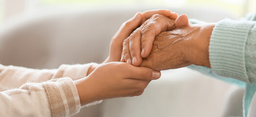 Senior woman with daughter holding hands at home, closeup