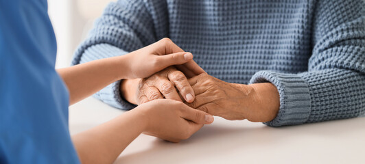 Caregiver with senior woman holding hands at table, closeup