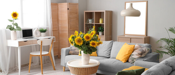 Stylish living room with grey sofas and vases of sunflowers bouquets on coffee table