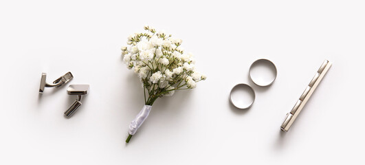 Wedding rings, tie clasp, cufflinks and boutonniere on white background. Top view