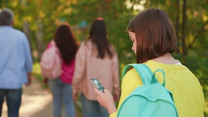 Child girl schoolgirl with backpack walking down street using smartphone. Close-up. Child communicates using smartphone. Teenage girl go with phone in hand outdoors. Modern technologies city life. © Victoriia