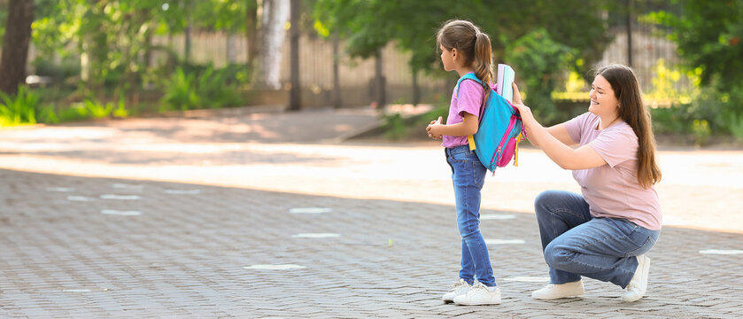 Mother with her daughter packing backpack for school outdoors