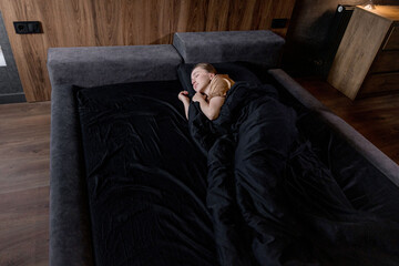 A woman is peacefully sleeping on a bed adorned with black sheets